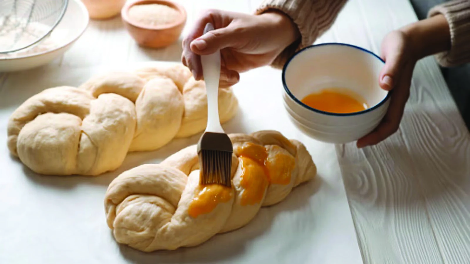 Freshly braided challah being brushed with egg wash