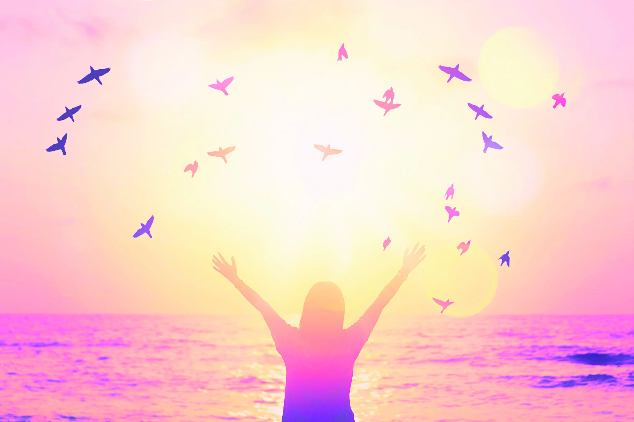 A woman raising her hands toward the sun by the ocean
